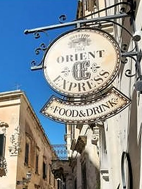 L'insegna ovale in ferro battuto di Orient Express: lettering slab su fondo avorio, la data 1984 sopra il monogramma e la targa curva Food & Drink.