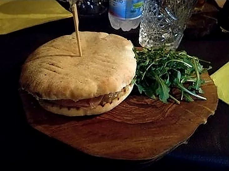 Puccia con bresaola, burrata e rucola servita su un tronchetto di legno.